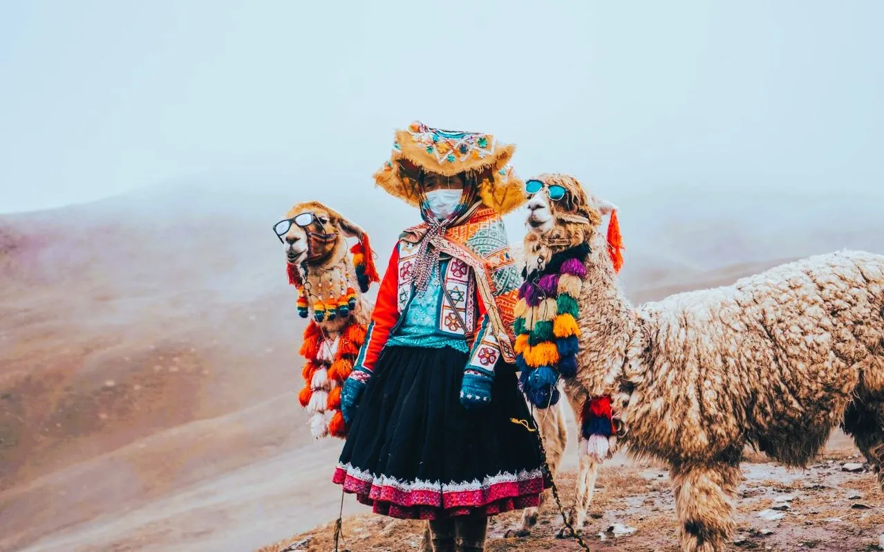 A woman in traditional clothes with a llama next to her on top of a mountain